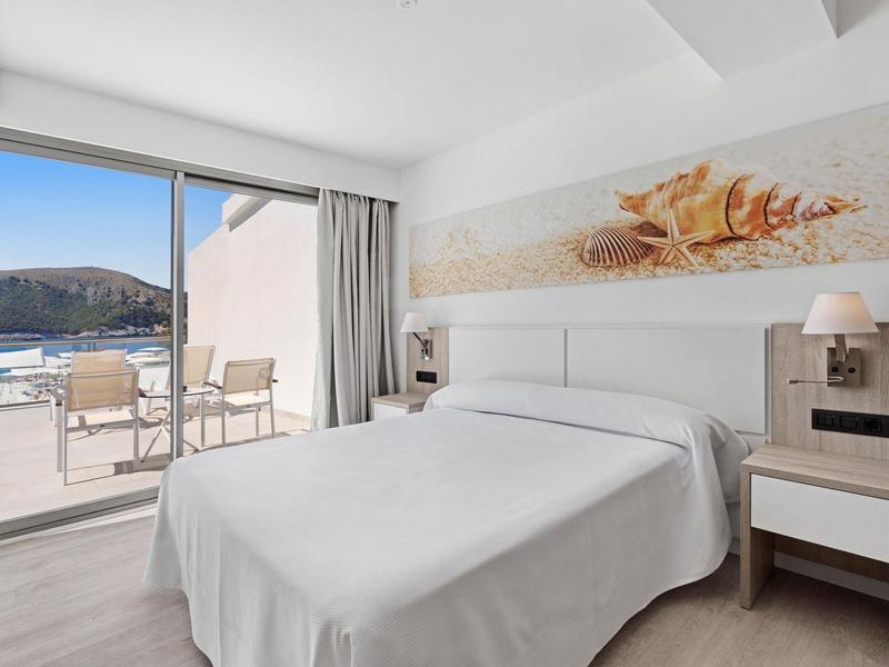 Chambre d'hôtel moderne avec grand lit blanc et terrasse offrant une vue sur la mer.