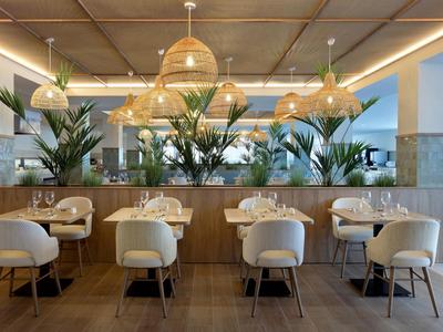 Nowoczesna restauracja hotelowa z drewnianymi stołami, białymi krzesłami i ozdobnymi lampami.
