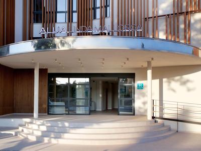 Wejście do hotelu z zaokrąglonymi schodami i przeszklonymi drzwiami pod zaokrąglonym daszkiem.