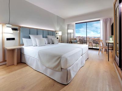 Nowoczesny pokój hotelowy z dużym łóżkiem podwójnym, balkonem i jasną drewnianą podłogą.