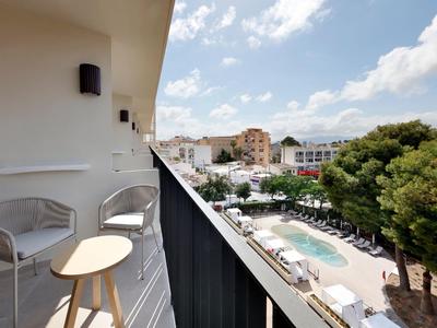 Balkon z krzesłami i stołem z widokiem na basen hotelowy i okoliczne budynki pod czystym niebem.