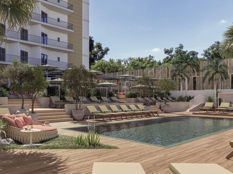 Modern outdoor pool with sun loungers and palm trees in a hotel area.