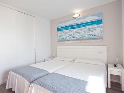 Camera d'hotel luminosa con letti singoli, mobili bianchi e quadro a tema mare.