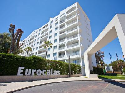 Moderno edificio alberghiero bianco a più piani con balconi sotto un cielo azzurro.
