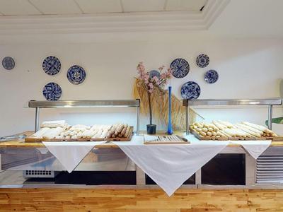 Tavolo buffet con pasticcini, pane e piatti decorativi appesi alla parete in una stanza luminosa.