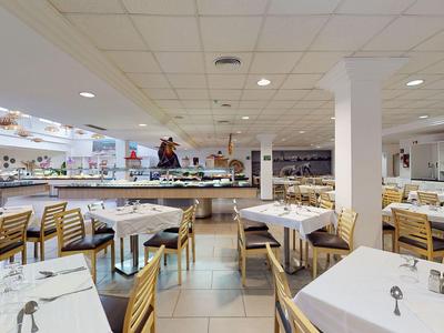 Ristorante spazioso con tovaglie bianche, sedie in legno e buffet sotto luci a soffitto luminose.