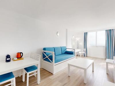 Camera d'hotel luminosa con divano blu, mobili bianchi e ampia finestra con tende.