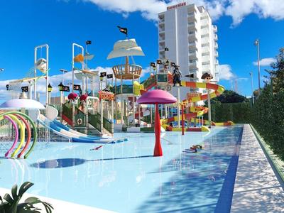 Parco acquatico all'aperto con scivoli e fontane a forma di fungo sotto un cielo blu vicino a un hotel alto.