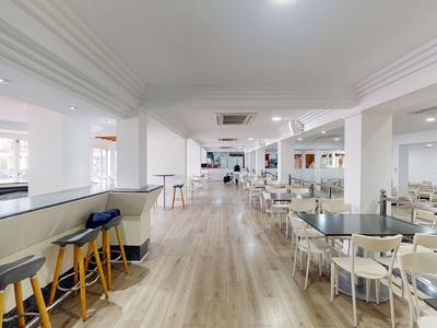 Ampia sala da pranzo dell'hotel luminosa con pavimento in legno, sgabelli al bar e sedie bianche attorno ai tavoli.