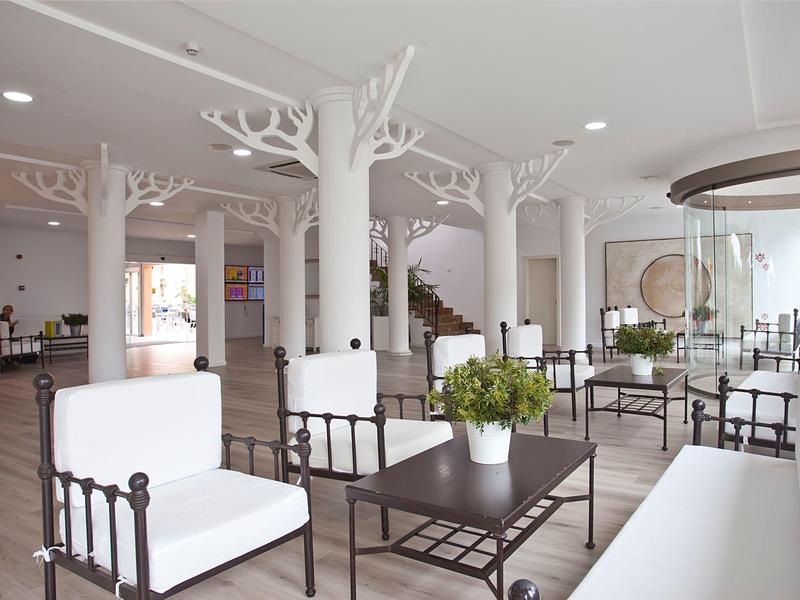 Luminoso ingresso con colonne bianche a forma di albero, sedie bianche, tavoli neri e piante verdi.