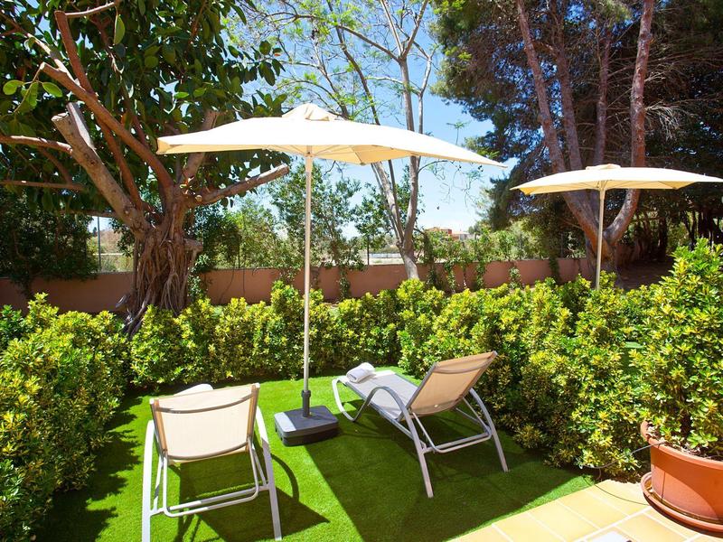 Due sdraio con ombrelloni in un giardino soleggiato circondato da vegetazione rigogliosa.