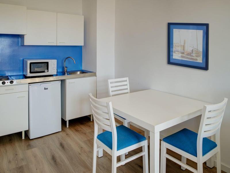 Piccola cucina bianca con paraschizzi blu, microonde, frigorifero e tavolo da pranzo con sedie blu.