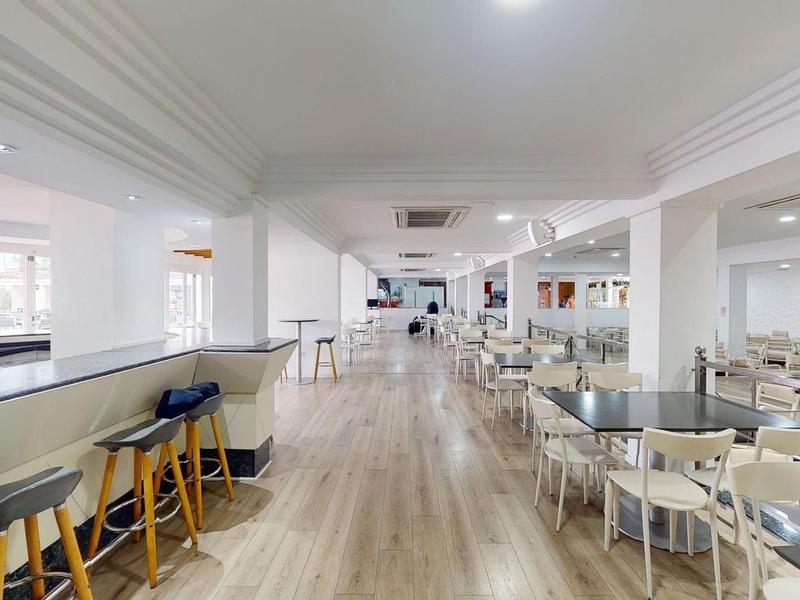 Ampia sala da pranzo dell'hotel luminosa con pavimento in legno, sgabelli al bar e sedie bianche attorno ai tavoli.