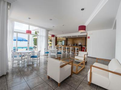 Lichte hotellounge met witte fauteuils, tafels en bar, uitzicht op terras en zee