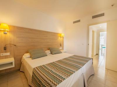 Schlafzimmer mit großem Doppelbett, Holzwand und modernen leuchtenden Wandlampen.