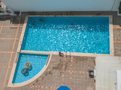 Vista aérea de una piscina con tumbonas y sombrillas en una terraza.