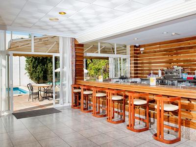 Moderner Barbereich mit langen Holzhockern und großen Glasfenstern zum Außenbereich mit Tisch und Pool.