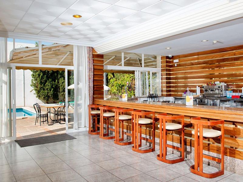 Moderner Barbereich mit langen Holzhockern und großen Glasfenstern zum Außenbereich mit Tisch und Pool.