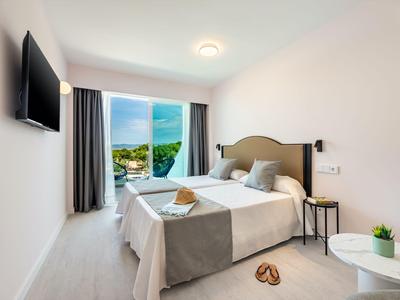 Modernes Hotelzimmer mit Doppelbett, Balkon und Meerblick bei klarem Himmel.