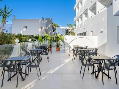 Außenbereich eines Hotels mit weißen Wänden, schwarzen Stühlen und Tischen auf einer hellen Terrasse.
