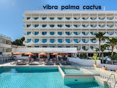 Moderner Hotelbau mit Pool, Sonnenschirmen und Palmen vor klarem Himmel.