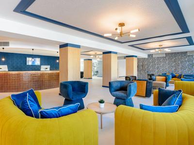 Heller Hotellobby mit gelben und blauen Sesseln, Rezeption und moderner Beleuchtung.