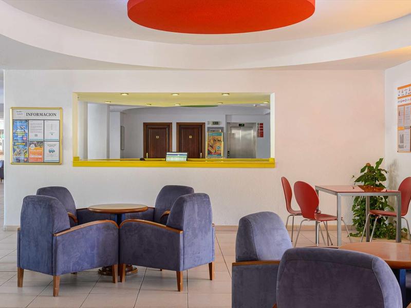 Moderne hotellobby met blauwe fauteuils, rode stoelen en een receptiebalie met een gele lijst.