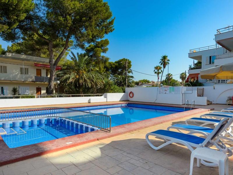 Modern buitenzwembad met ligstoelen en witte gebouwen onder een heldere hemel