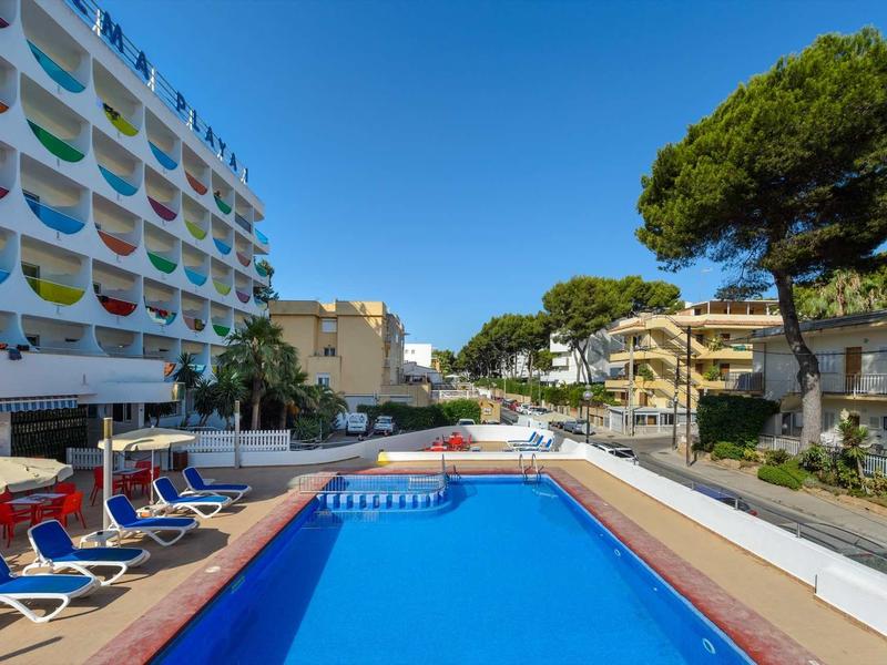 Hotel met buitenzwembad, ligstoelen en meerlaagse gebouwen onder een heldere blauwe lucht.