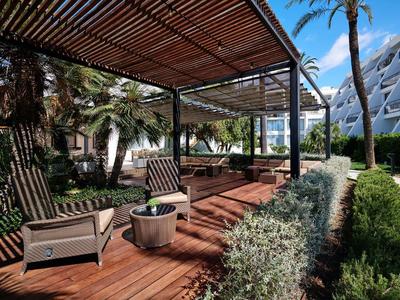 Terrazza in legno con poltrone sotto una pergola in un giardino tropicale dell'hotel.