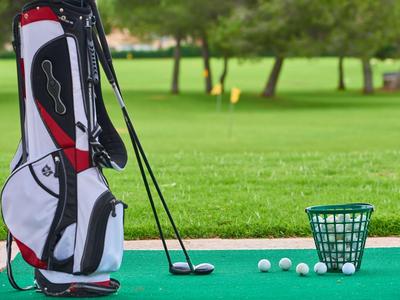 Golfutensilien mit Tasche, Schlägern, Bällen und Korb auf einem grünen Übungsbereich
