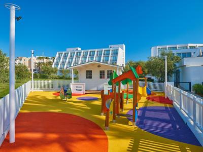 Area giochi colorata con scivolo vicino a un hotel moderno sotto un cielo azzurro.