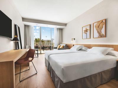 Camera d'hotel moderna con due letti, scrivania e balcone con vista sulle palme.