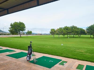 Golfplatz mit Trainingsbereich und Blick auf eine Wasserfläche unter klarem Himmel.