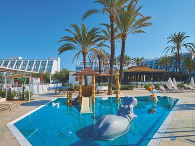 Hotelpool mit Wasserspielplatz, Rutschen und Palmen unter klarem blauem Himmel.