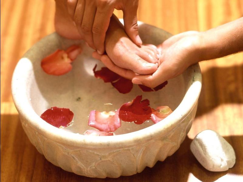 Mani che si tengono sopra una ciotola d'acqua con petali di rosa per un trattamento spa.