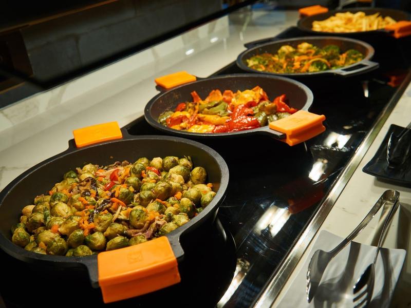 Buffet con diversi piatti caldi serviti in pentole su un bancone nero.