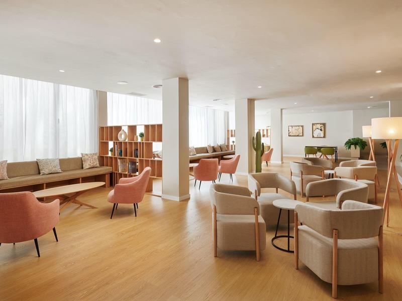 Sala d'hotel luminosa con poltrone, divani e pavimento in legno chiaro.