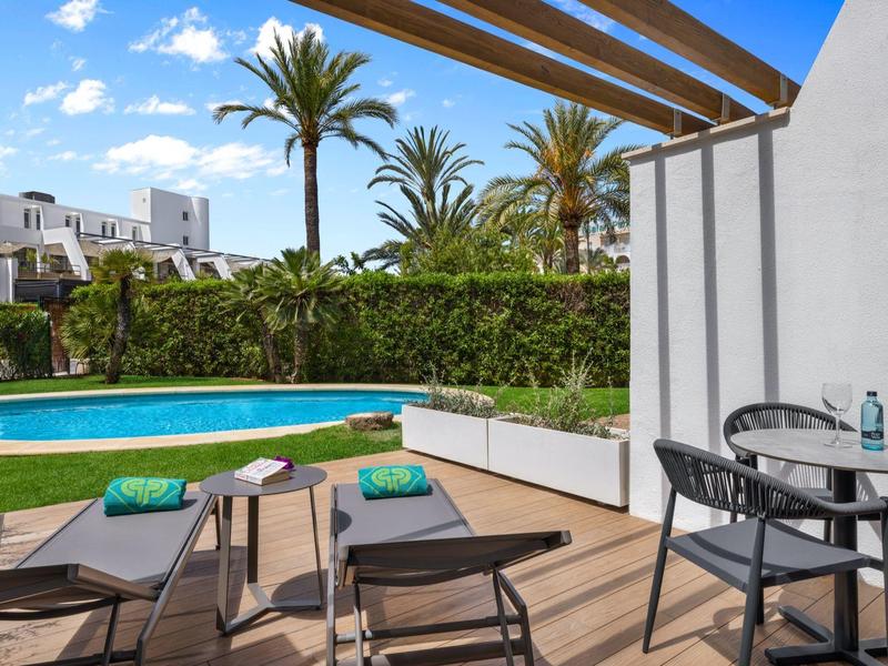 Terrazza d'hotel con piscina, lettini prendisole e tavolo rotondo sotto pergola.