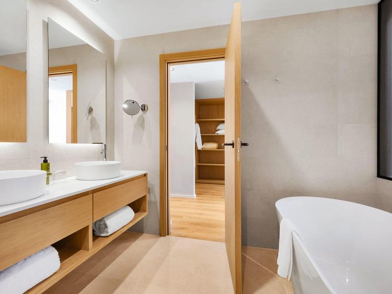 Bagno moderno con vasca, doppio lavabo e porta aperta verso la camera da letto.