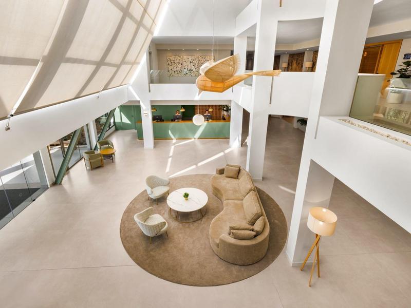 Salotto d'hotel moderno con mobili beige e grandi finestre luminose.