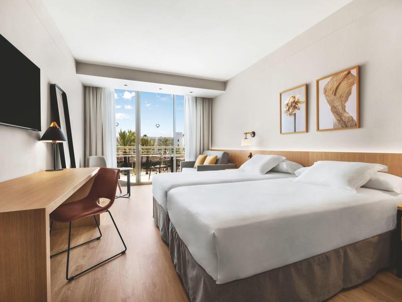 Camera d'hotel moderna con due letti, scrivania e balcone con vista sulle palme.