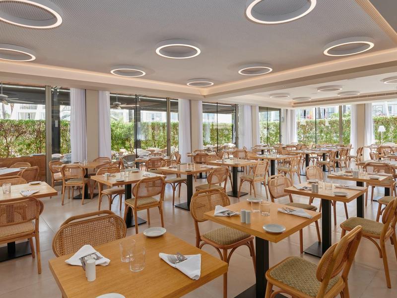 Sala da pranzo luminosa con grandi finestre e tavoli in legno apparecchiati.