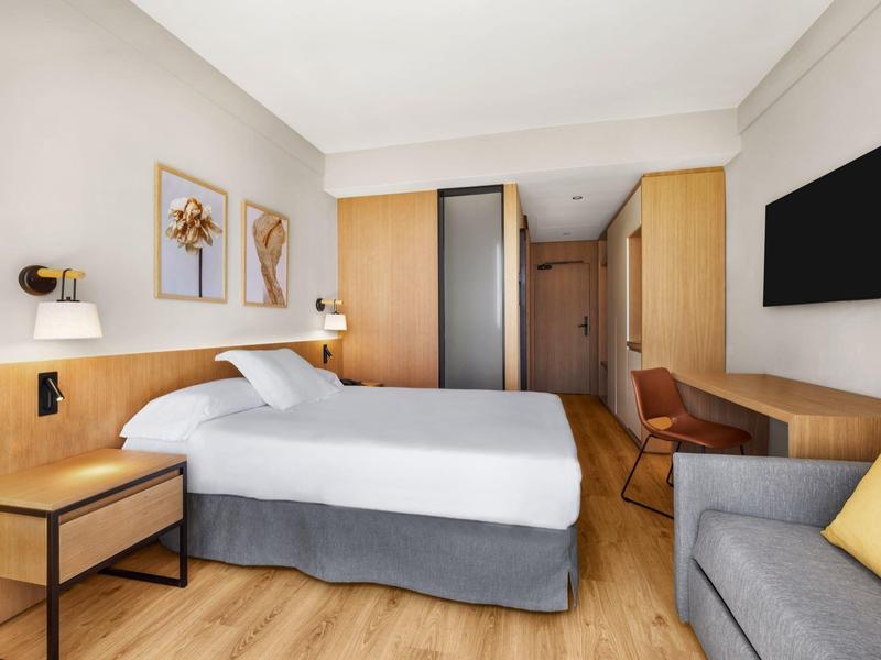 Camera d'hotel moderna con letto matrimoniale, scrivania, TV a parete e decorazioni.