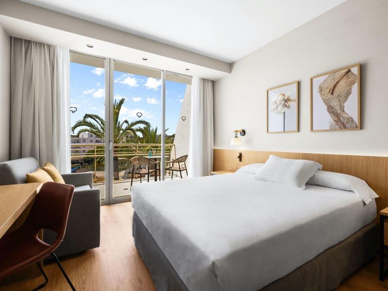 Camera d'hotel moderna con letto matrimoniale, scrivania, terrazza e vista sulla natura.