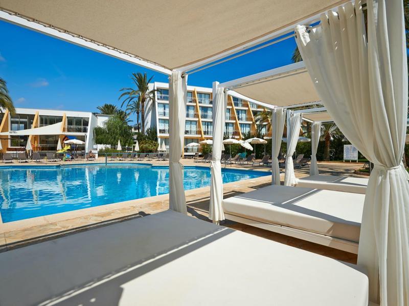 Area piscina del resort con lettini e tende bianche sotto un cielo blu terso.