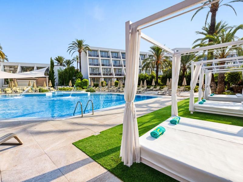 Area piscina dell'hotel con lettini, gazebo e architettura moderna sotto cielo azzurro