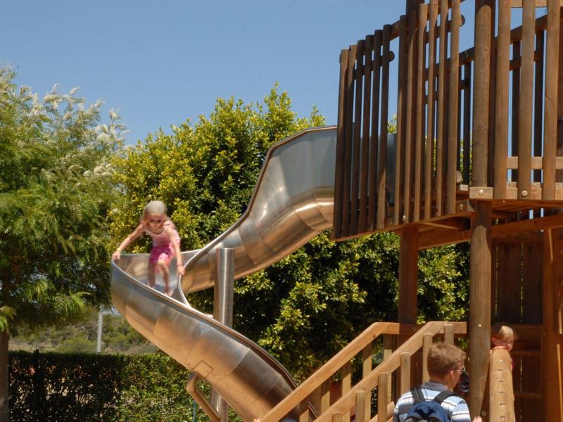 Bambini che giocano su uno scivolo di metallo in un parco all'aperto con cielo sereno.