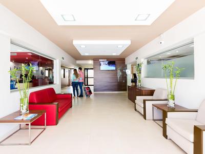 Světlá hotelová hala s bílými stěnami, červenou pohovkou a moderním osvětlením.