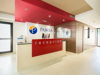 Moderní recepce s červeným akcentem a logem na stěně v jasné hotelové chodbě.